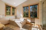 Indulge in relaxation in this luxurious bathroom, featuring a spacious soaking tub perfectly positioned to offer serene views of the surrounding pine forest through large windows.