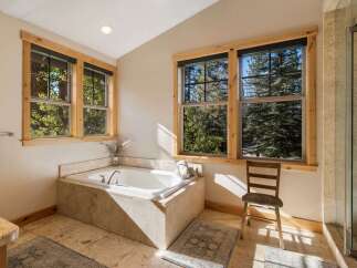 Indulge in relaxation in this luxurious bathroom, featuring a spacious soaking tub perfectly positioned to offer serene views of the surrounding pine forest through large windows.