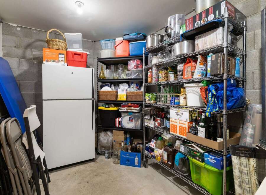 Discover ample storage solutions in this property's basement, featuring a large white refrigerator and extensive shelving units.