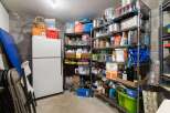 Discover ample storage solutions in this property's basement, featuring a large white refrigerator and extensive shelving units.
