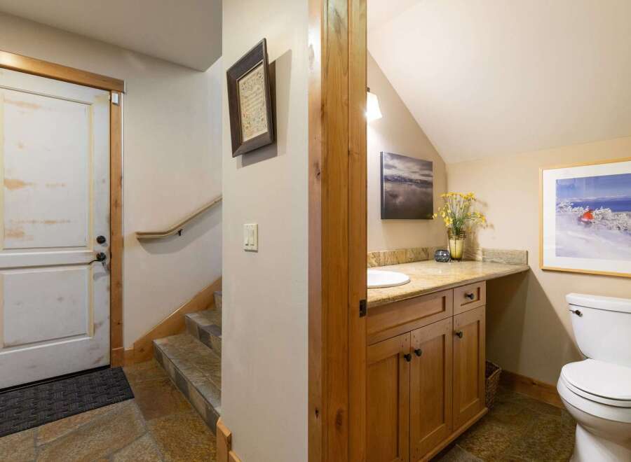 This charming bathroom features a wooden vanity with a granite countertop and a white sink, complemented by a large framed ski poster on the wall.