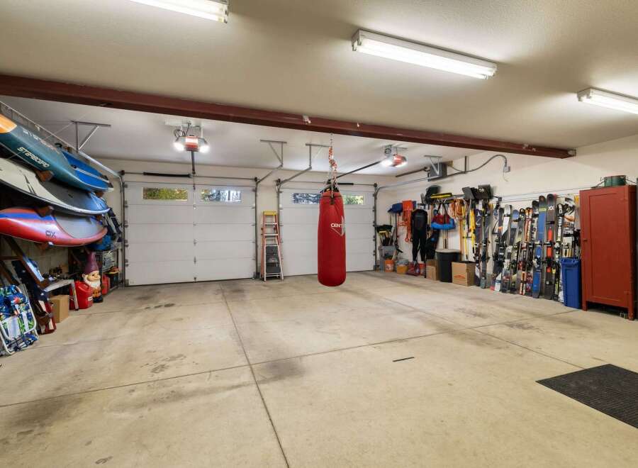 This spacious garage offers ample storage for all your recreational gear, including multiple paddleboards neatly stacked and a collection of skis ready for the slopes.