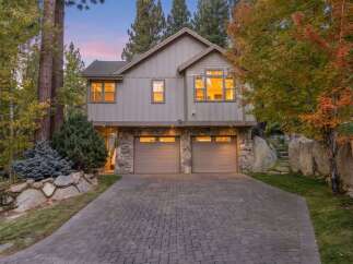 This stunning home features a modern exterior with a stone-accented lower level and a light gray siding.