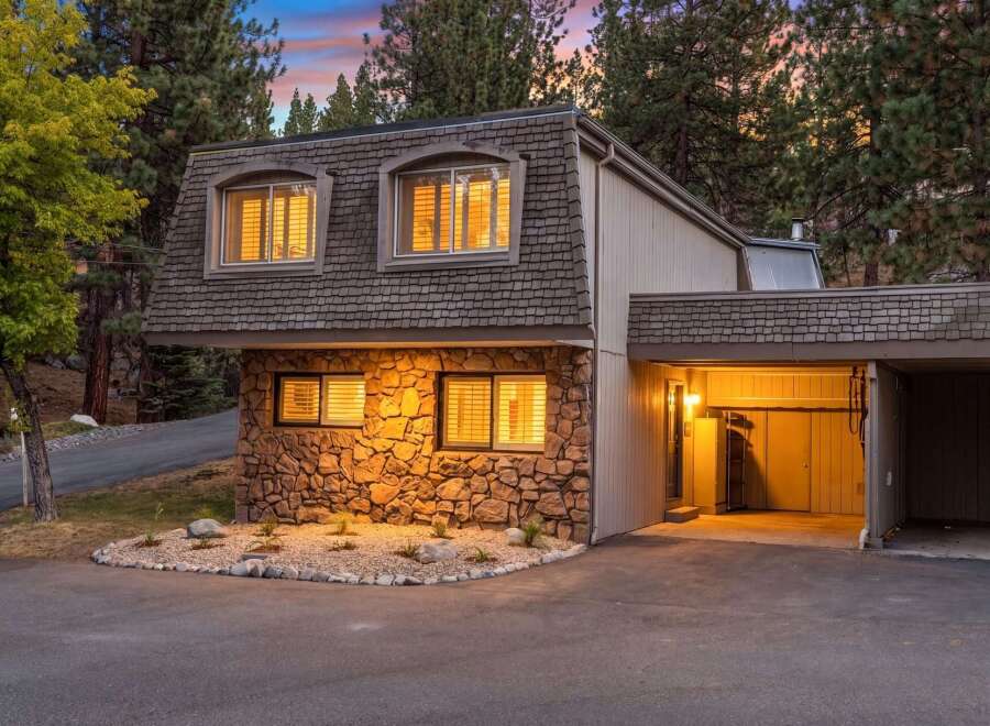 Nestled amongst tall pine trees, this charming home features a unique stone facade and a mansard roof.