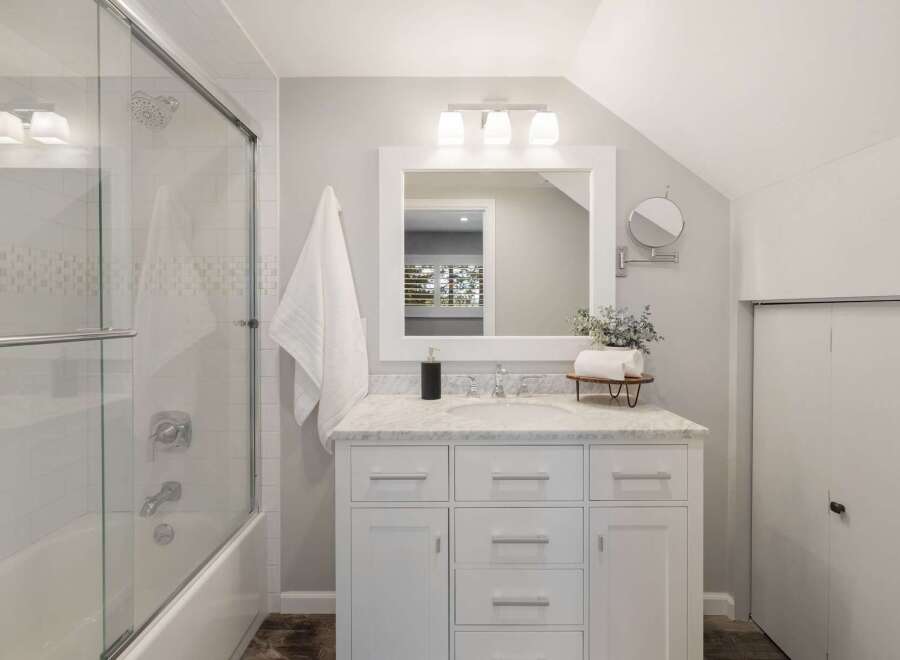 This modern bathroom features a sleek white vanity with marble countertops, complemented by a large framed mirror and a trio of vanity lights.