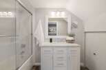 This modern bathroom features a sleek white vanity with marble countertops, complemented by a large framed mirror and a trio of vanity lights.