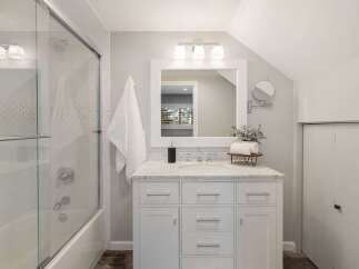 This modern bathroom features a sleek white vanity with marble countertops, complemented by a large framed mirror and a trio of vanity lights.