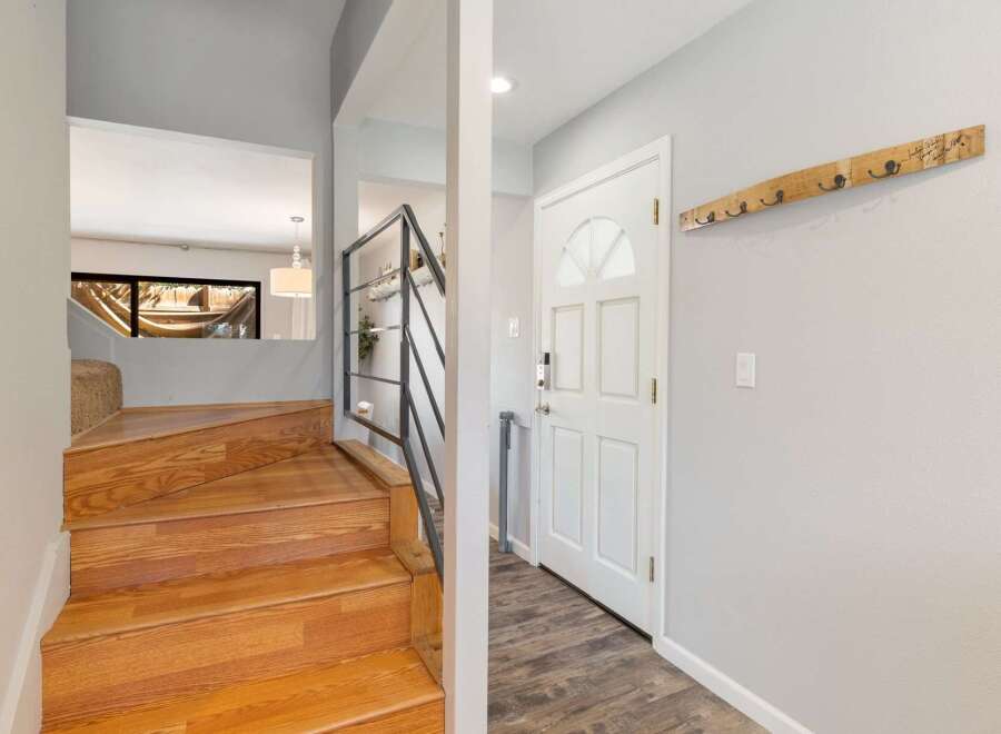 Step into a welcoming entryway featuring a beautiful wooden staircase and a stylish coat rack mounted on a light gray wall.