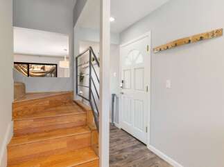 Step into a welcoming entryway featuring a beautiful wooden staircase and a stylish coat rack mounted on a light gray wall.