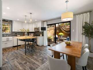 This modern kitchen features white cabinetry, a decorative backsplash, and a butcher block island with bar stools.