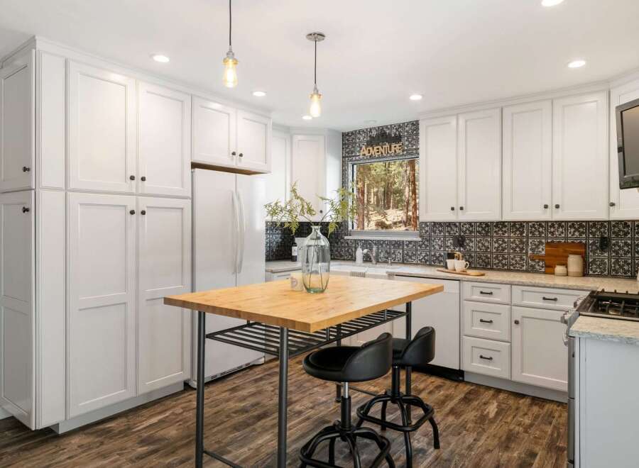 This charming kitchen boasts pristine white cabinetry offering ample storage, complemented by a stylish black and white tiled backsplash.