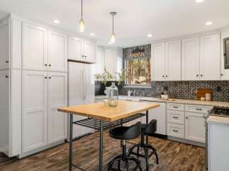 This charming kitchen boasts pristine white cabinetry offering ample storage, complemented by a stylish black and white tiled backsplash.