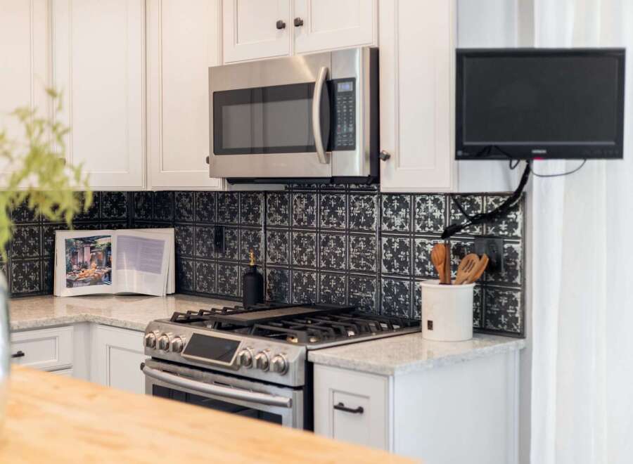 This modern kitchen features a sleek stainless steel microwave above a gas range, complemented by a decorative black tile backsplash.