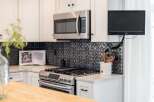 This modern kitchen features a sleek stainless steel microwave above a gas range, complemented by a decorative black tile backsplash.