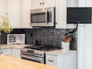 This modern kitchen features a sleek stainless steel microwave above a gas range, complemented by a decorative black tile backsplash.