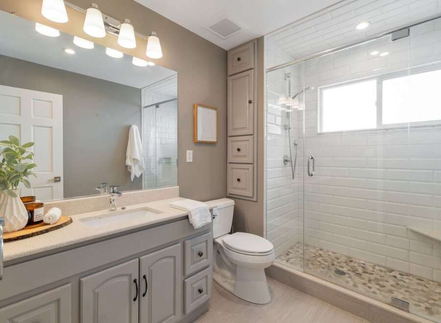 This modern bathroom features a sleek vanity with a speckled countertop and ample storage, complemented by a spacious walk-in shower with white subway tile and a pebble floor.
