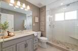 This modern bathroom features a sleek vanity with a speckled countertop and ample storage, complemented by a spacious walk-in shower with white subway tile and a pebble floor.