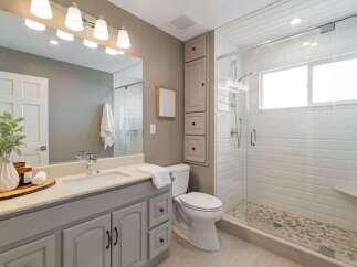 This modern bathroom features a sleek vanity with a speckled countertop and ample storage, complemented by a spacious walk-in shower with white subway tile and a pebble floor.