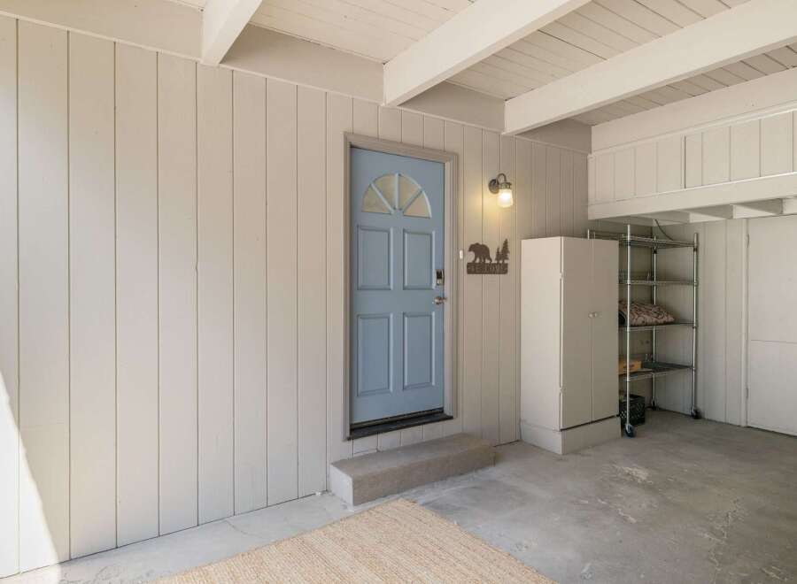 Step into this charming entryway featuring a welcoming light blue door adorned with a rustic bear and tree 'Welcome' sign.