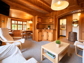 Step into a warm and inviting living space, featuring rich wood paneling throughout and a cozy dining area bathed in natural light from large windows.