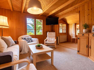 Experience cozy living in this charming wooden cabin, featuring a comfortable living area with a sofa, armchair, and coffee table.