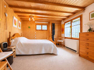 Experience cozy living in this charming wooden-paneled bedroom, featuring a comfortable queen-sized bed with a plush white comforter.