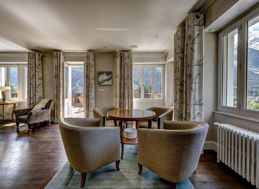 Experience breathtaking mountain views from this elegant living space, featuring a cozy seating area with plush armchairs and a central wooden table.