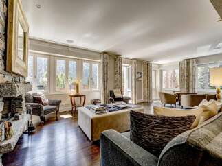 Experience luxurious mountain living in this spacious living room, featuring a grand stone fireplace and large windows that offer breathtaking views of the surrounding landscape.