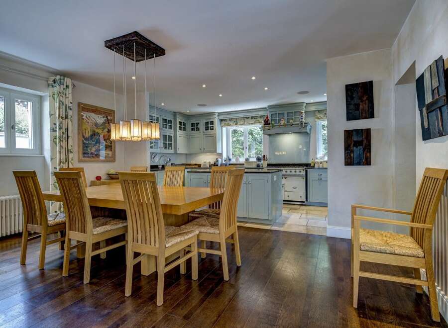 This spacious open-plan kitchen and dining area features a large wooden dining table with six chairs, illuminated by a modern chandelier.