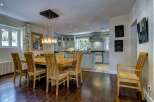 This spacious open-plan kitchen and dining area features a large wooden dining table with six chairs, illuminated by a modern chandelier.