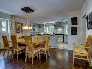 This spacious open-plan kitchen and dining area features a large wooden dining table with six chairs, illuminated by a modern chandelier.