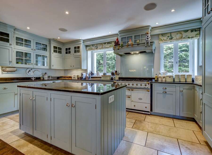 This spacious kitchen features custom light blue cabinetry with glass-fronted upper cabinets and a large central island with a dark granite countertop.