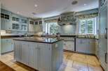 This spacious kitchen features custom light blue cabinetry with glass-fronted upper cabinets and a large central island with a dark granite countertop.