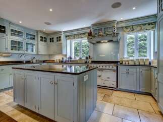 This spacious kitchen features custom light blue cabinetry with glass-fronted upper cabinets and a large central island with a dark granite countertop.