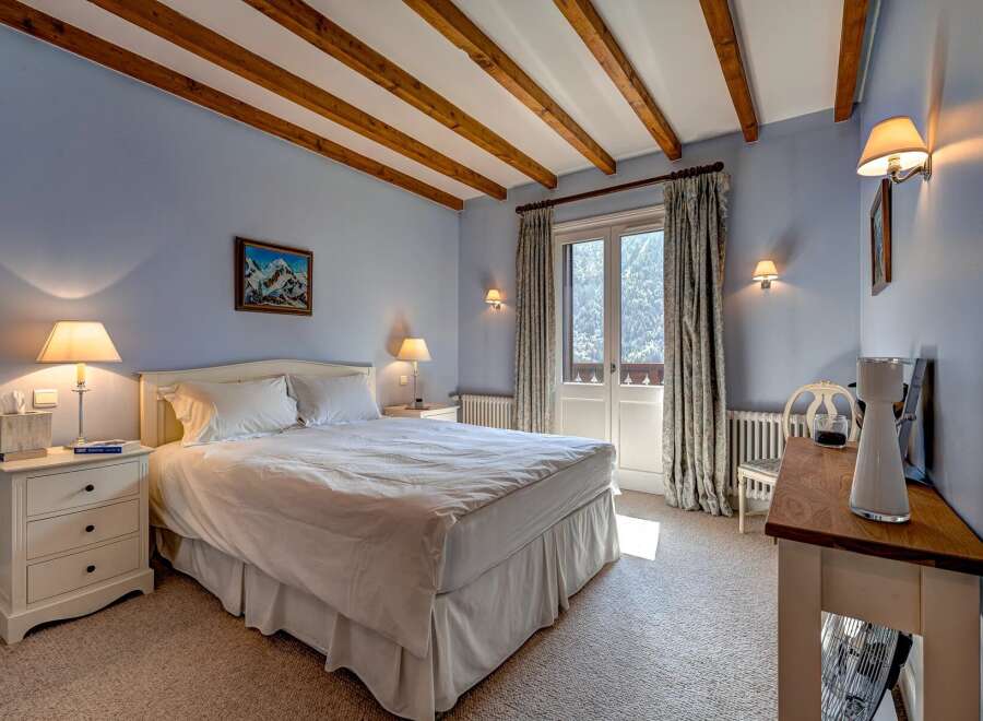 Experience alpine charm in this cozy bedroom featuring exposed wooden beams and a serene blue color palette.