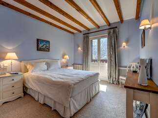 Experience alpine charm in this cozy bedroom featuring exposed wooden beams and a serene blue color palette.