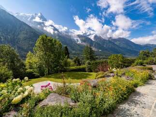 Experience breathtaking mountain views from this stunning property, featuring a lush green lawn and vibrant flower gardens.