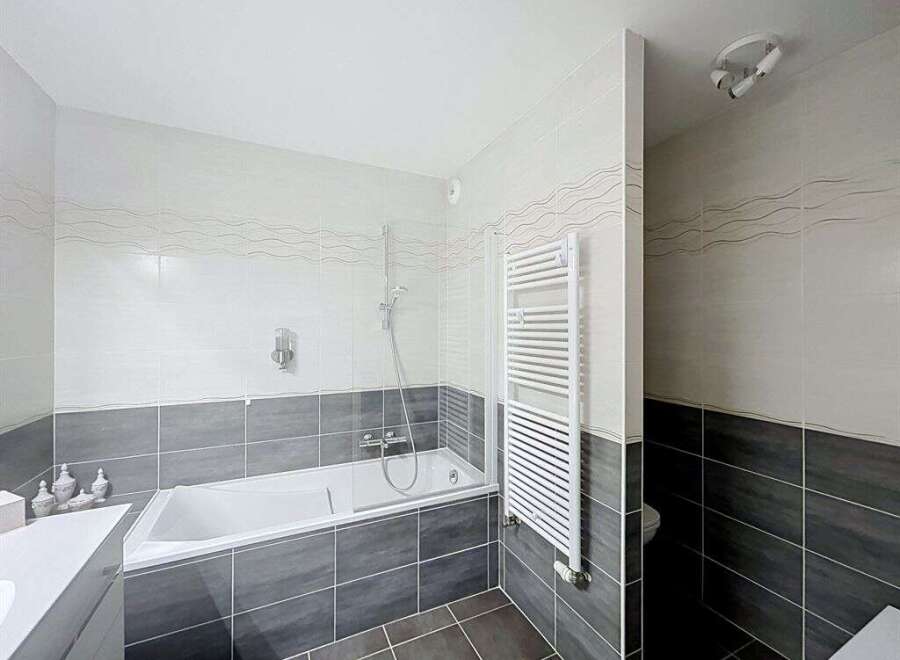 This modern bathroom features a sleek white bathtub with a glass shower screen, perfect for relaxing soaks.