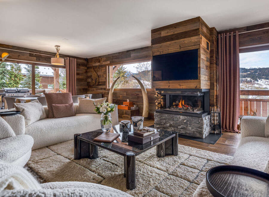 Experience luxury mountain living in this stunning chalet living room, featuring a modern fireplace and a large TV mounted on a rustic wood accent wall.