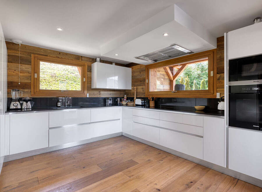 Experience modern luxury in this stunning chalet kitchen, featuring sleek white cabinetry and a dramatic wood-paneled accent wall.