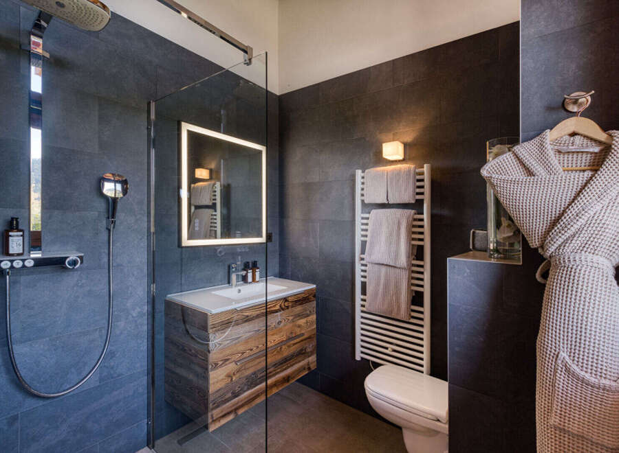 Experience luxury in this modern bathroom, featuring a sleek walk-in shower with a rainfall showerhead and a stylish vanity with a wooden finish.