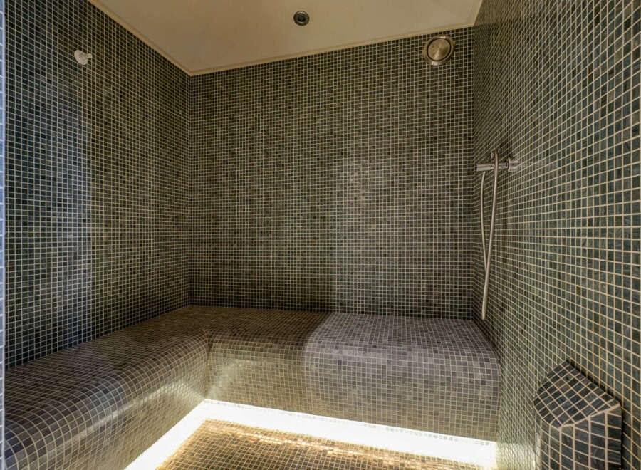 Experience ultimate relaxation in this luxurious steam room, featuring sleek mosaic tilework and comfortable, built-in seating.