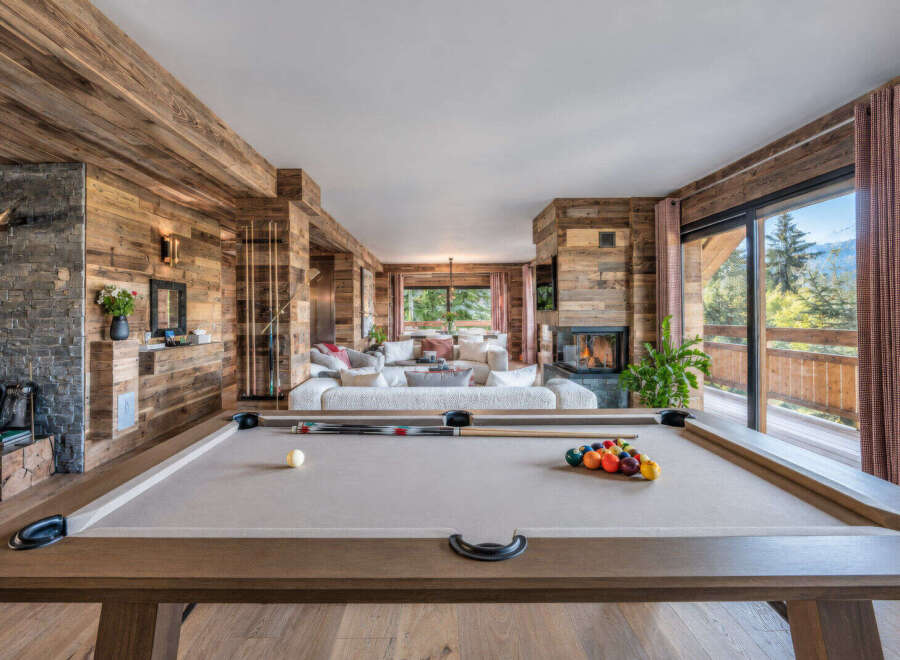 Experience luxury mountain living in this stunning chalet, featuring a spacious open-plan living area with a cozy fireplace and a modern pool table for entertainment.