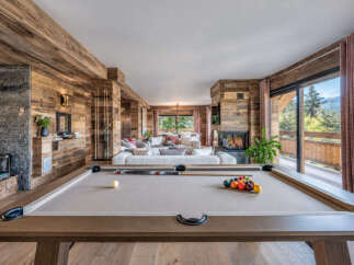 Experience luxury mountain living in this stunning chalet, featuring a spacious open-plan living area with a cozy fireplace and a modern pool table for entertainment.