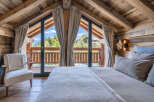 Experience rustic luxury in this charming chalet bedroom, featuring a cozy bed and a comfortable armchair.