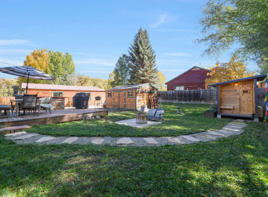 Enjoy outdoor living in this charming backyard featuring a spacious wooden deck with a dining set and umbrella, perfect for al fresco meals.