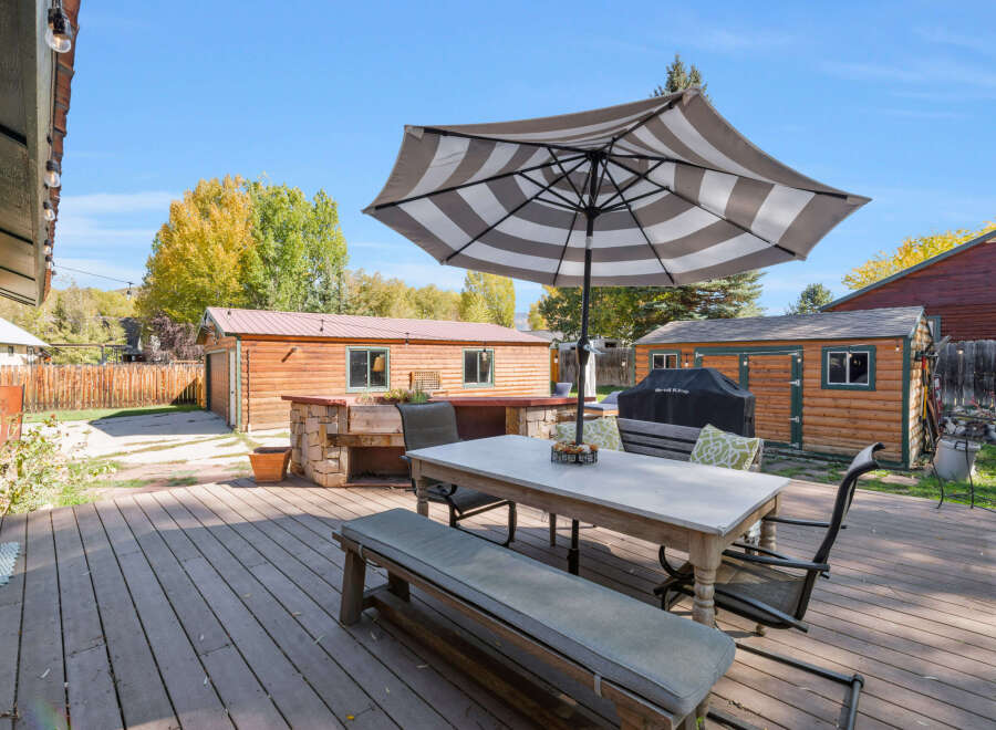 Enjoy outdoor living with this spacious deck featuring a dining set under a striped umbrella, perfect for al fresco meals.