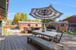 Enjoy outdoor living with this spacious deck featuring a dining set under a striped umbrella, perfect for al fresco meals.
