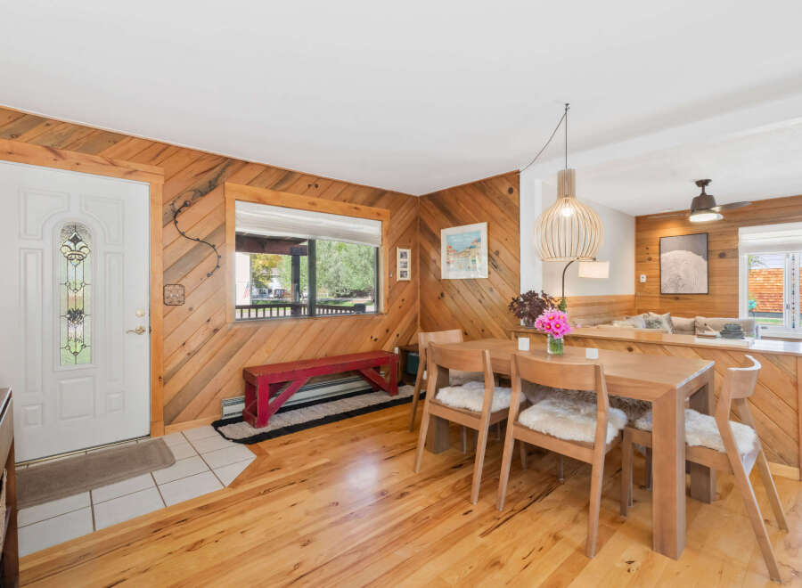 Step into a warm and inviting living space featuring a charming dining area with a light wood table and chairs adorned with cozy sheepskin cushions.
