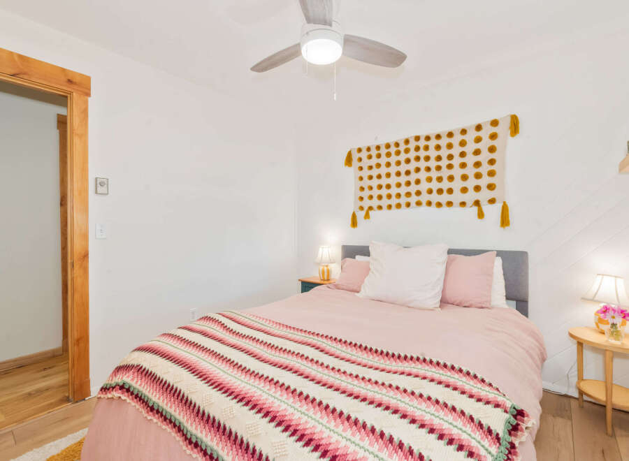 This charming bedroom features a cozy queen-size bed adorned with soft pink linens and a vibrant, patterned throw blanket.